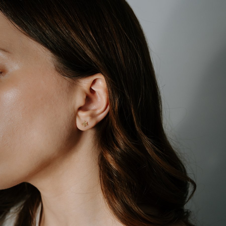 Zbliżenie na ucho kobiety z kolczykiem w kształcie gwiazdy z 14-karatowego złota.