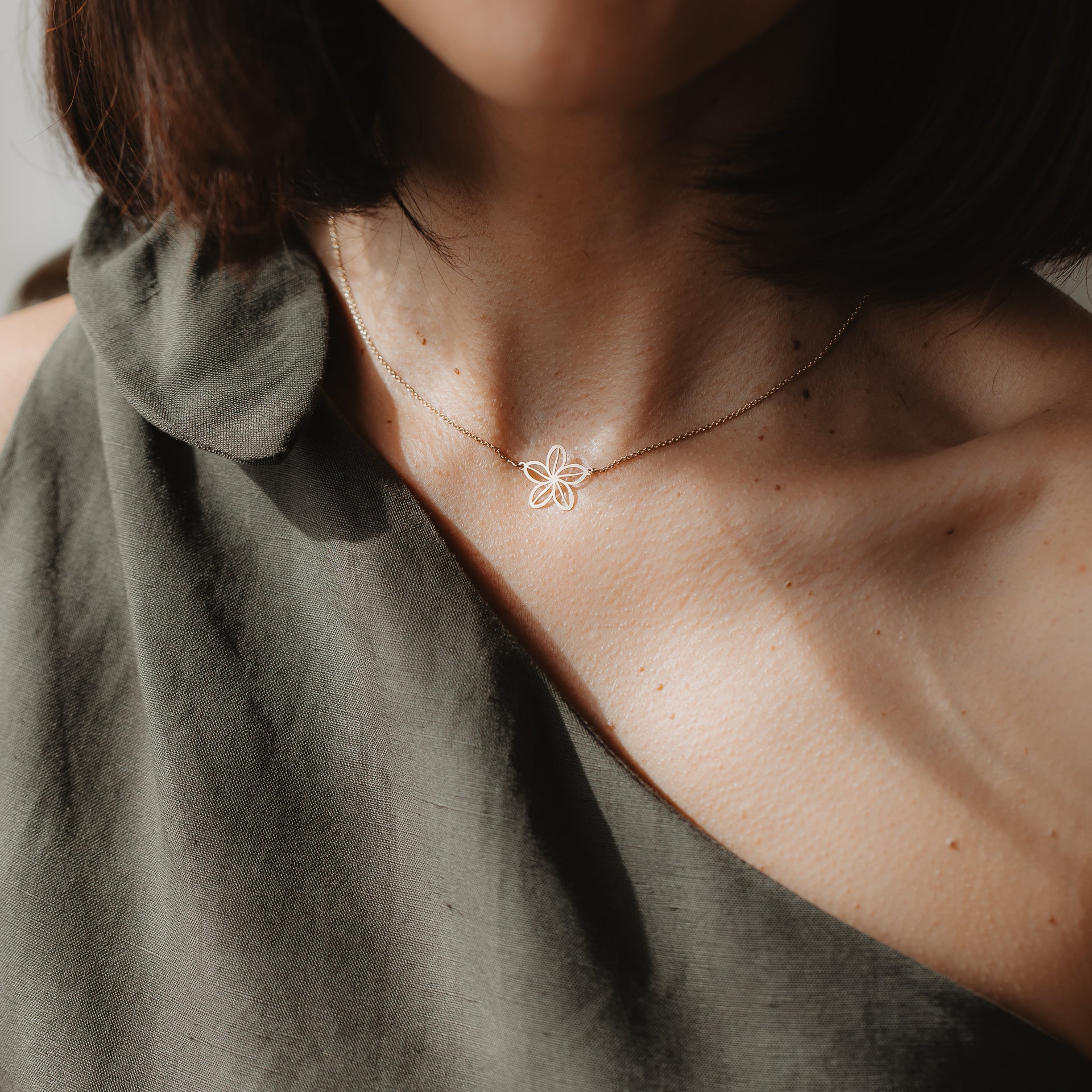 Zbliżenie modelki w naszyjniku Wildflower z żółtego złota 14K z delikatną zawieszką w kształcie konturu kwiatu, sfotografowanym na obojczyku w naturalnym świetle.