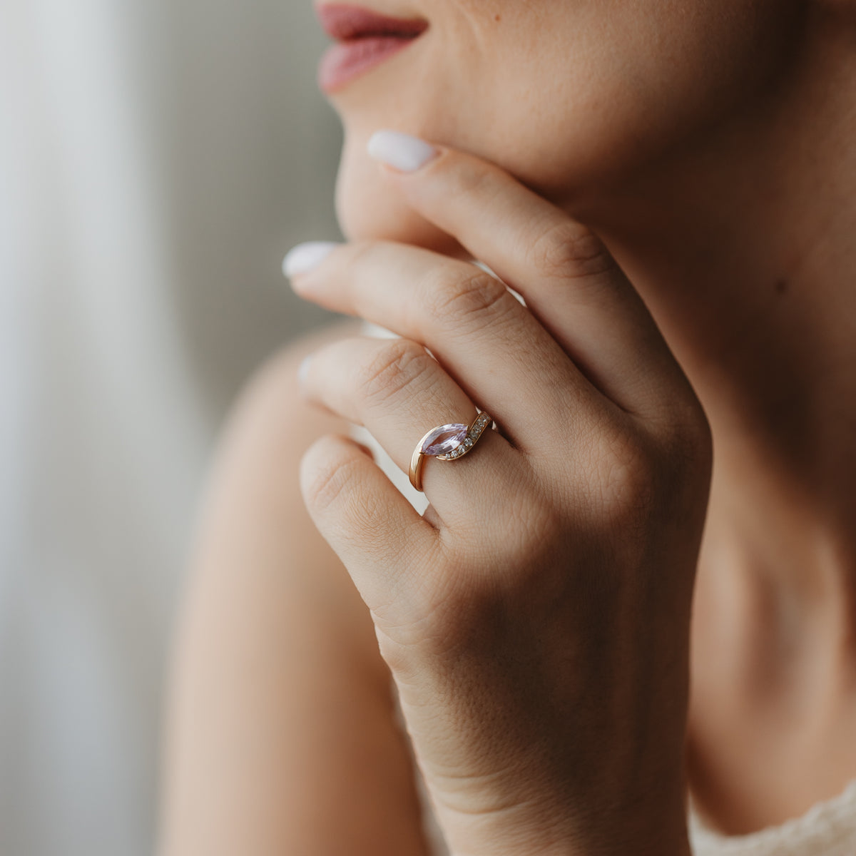 Zbliżenie dłoni przy twarzy z pierścionkiem Velvet Rose z żółtego złota 14K z różowym szafirem w szlifie markiza i drobnymi diamentami akcentowymi.