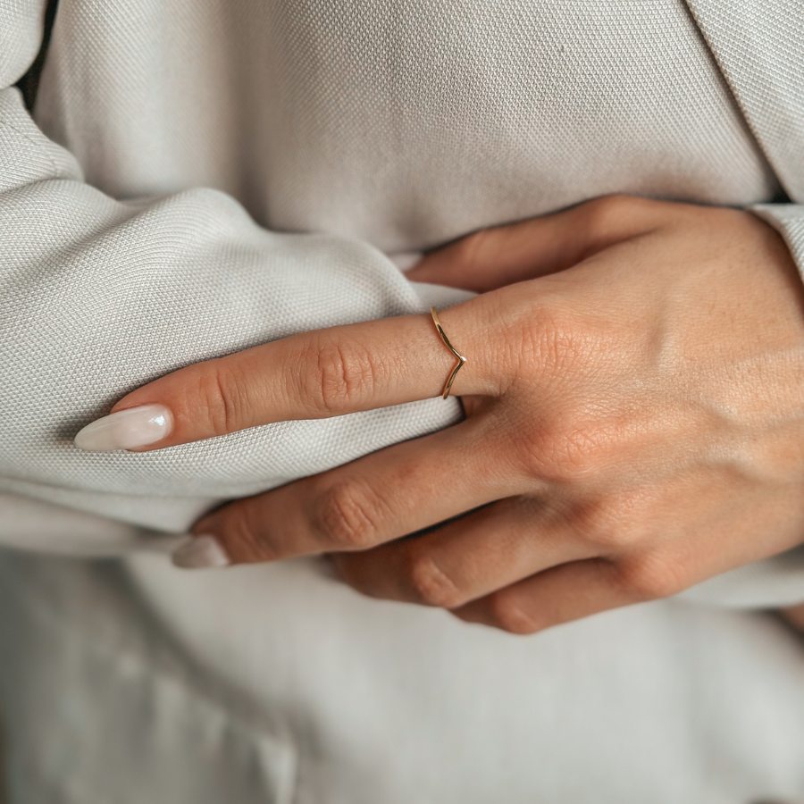 Zbliżenie dłoni z minimalistycznym, pozłacanym srebrnym pierścionkiem na tle jasnej tkaniny.