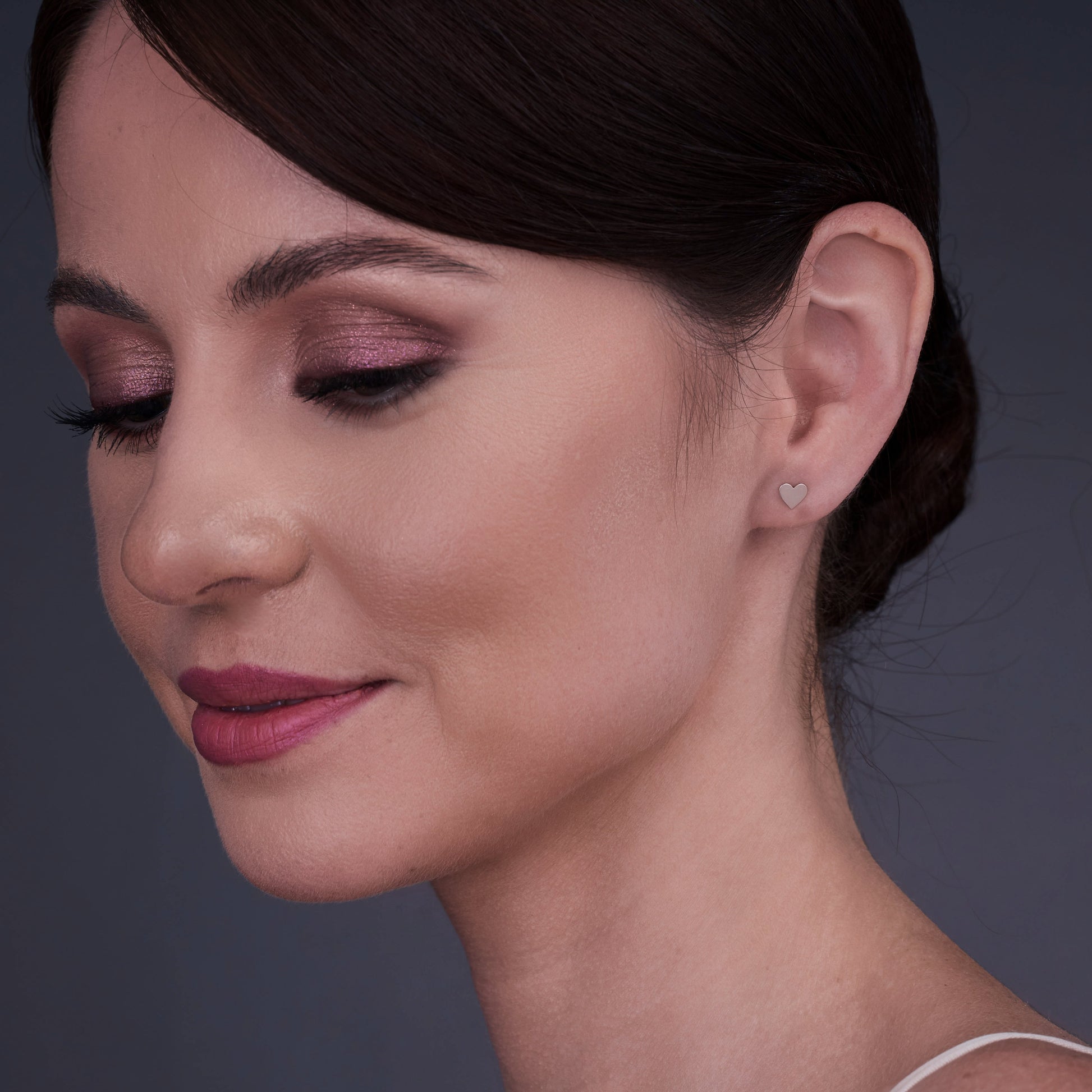 Kobieta nosząca kolczyki w kształcie serca z 14-karatowego złota, z zamkniętymi oczami i spokojnym wyrazem twarzy.