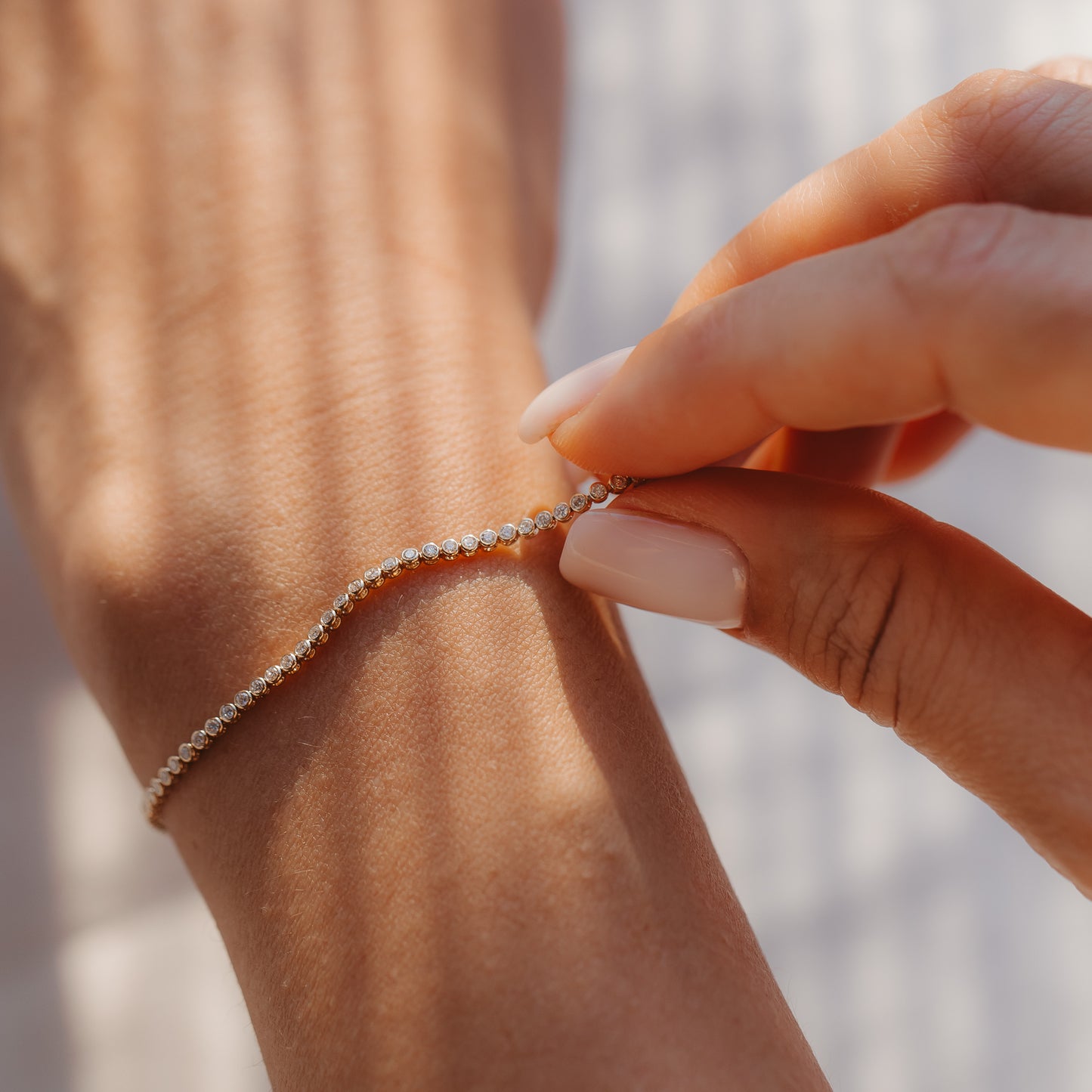 Zbliżenie dłoni zapinającej na nadgarstku tenisową bransoletkę z żółtego złota 14K z diamentami w ciepłym świetle słonecznym.