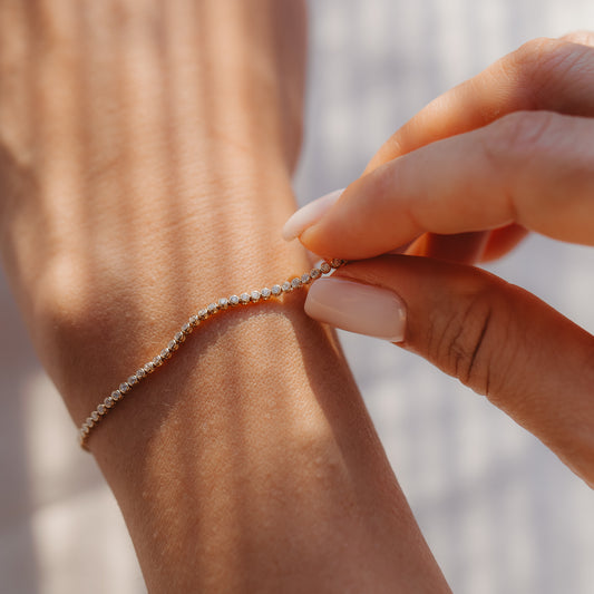 Zbliżenie dłoni zapinającej na nadgarstku tenisową bransoletkę z żółtego złota 14K z diamentami w ciepłym świetle słonecznym.