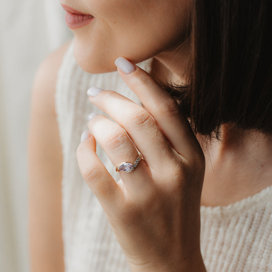 Zbliżenie dłoni z pierścionkiem zaręczynowym z żółtego złota 14k z szafirem w szlifie markiza i diamentami, przy twarzy w miękkim, naturalnym świetle.
