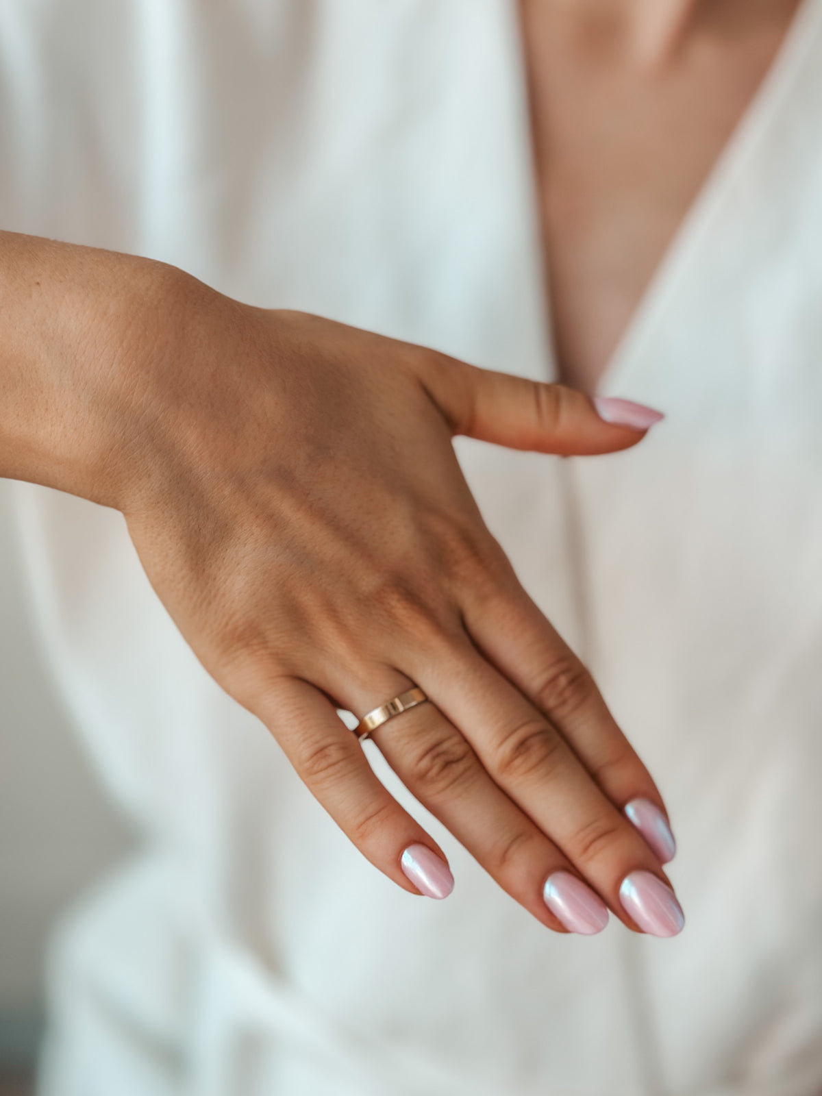 Dłoń prezentująca prostą złotą obrączkę ślubną z różowym manicure.