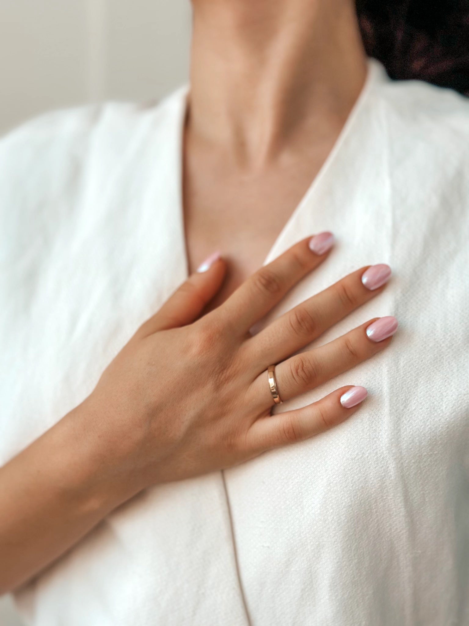 Zbliżenie dłoni z manicurem spoczywającej na piersi, na której znajduje się szeroka złota obrączka ślubna.